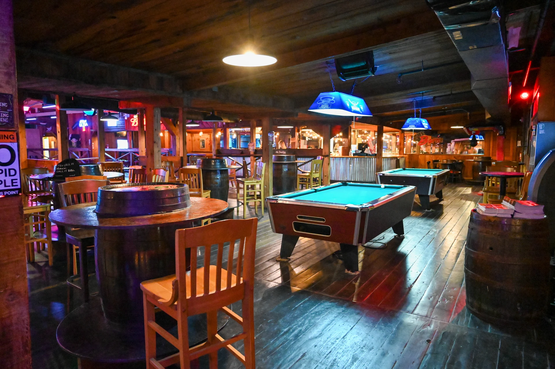 Pool tables and barrel seating inside The Barn under evening lights